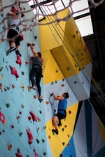 A group of people learning how to do rope climbing at a climbing wall indoors